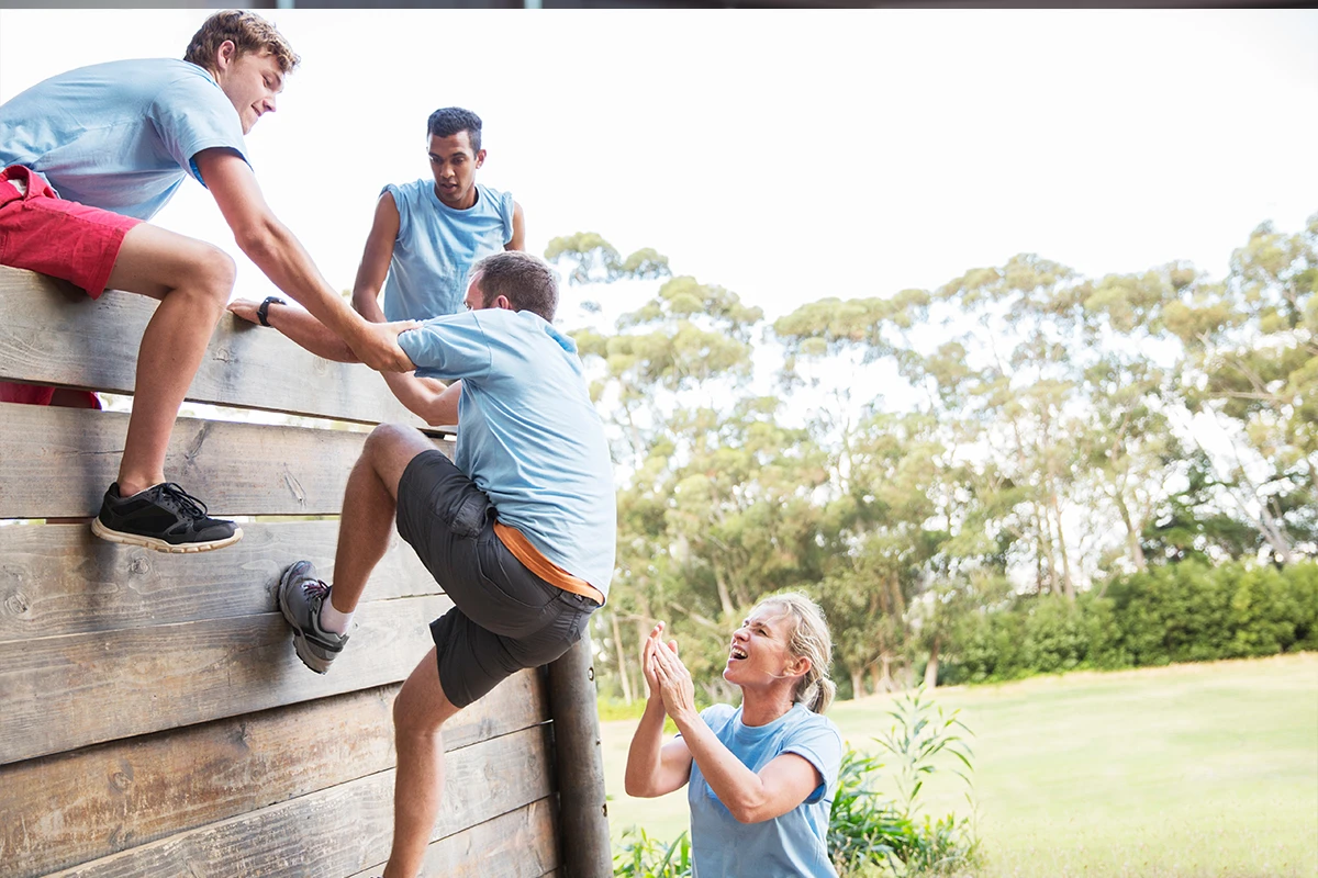 Firmenfitness - Teambuilding, Gruppe von Menschen erklimmt Holzwall